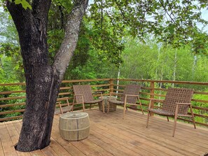 A wooden deck with wicker furniture and a round table, surrounded by a railing with a view of a forest.