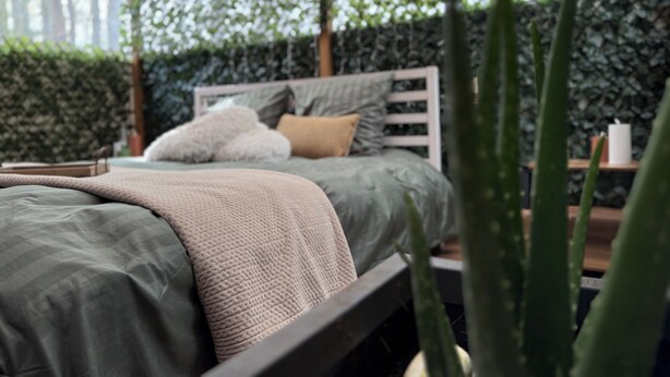 A bed with a green bedspread, a white headboard, and a textured throw blanket.