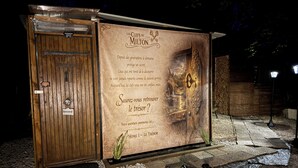 A wooden structure with a signboard, a door, and a small garden area.