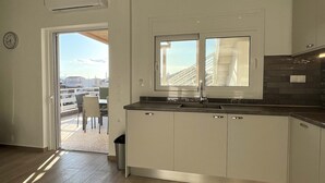 A modern kitchen with a window, white cabinets, and a view of the city. - Taygetos View - Bright Modern Retreat in Center (Kalamata)