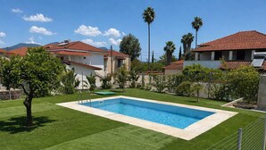 Une piscine rectangulaire bordée de blanc, entourée d’une pelouse verdoyante et d’une clôture en métal.