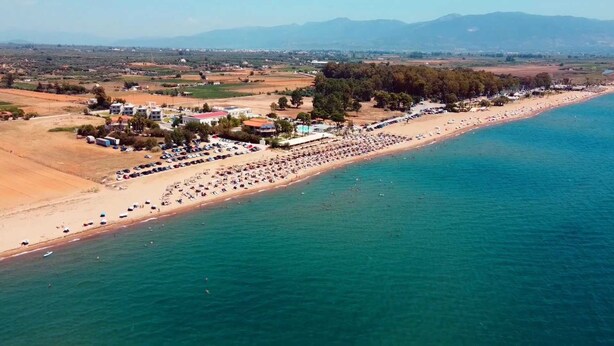 Vue aérienne d’une zone côtière avec une plage, des voitures garées et des bâtiments.