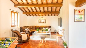 A cozy living room with a leather sofa, a foosball table, a coffee table with decorative items, a TV, and a wooden ceiling. - Villa La Bergerie by Villa Plus (Saint-Cézaire-sur-Siagne)