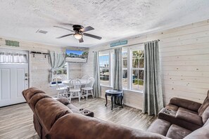 Una habitación con ventilador de techo, televisión, una mesa de comedor con sillas y un sofá.