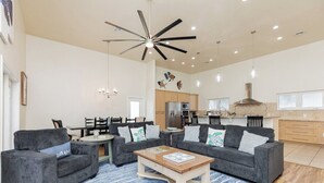 A spacious living room with a large sofa set, a coffee table, and a dining area with chairs and a table.