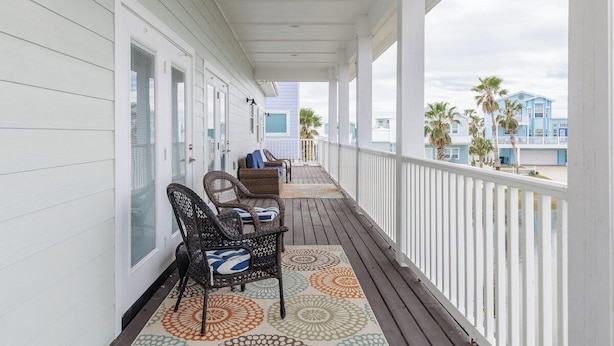 A covered porch with a railing, wicker chairs, and a patterned rug.
