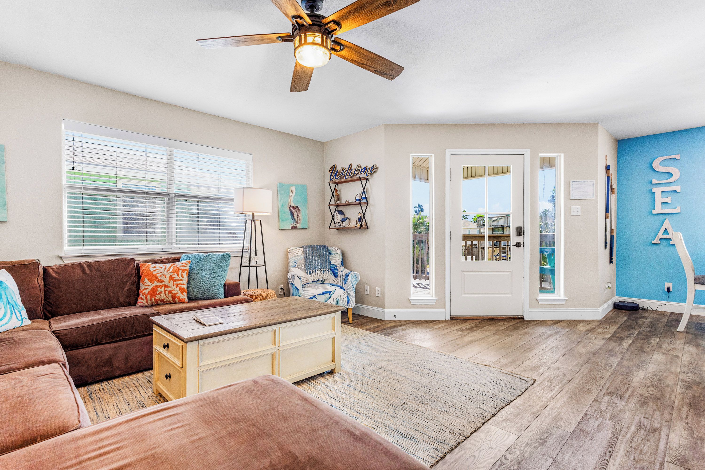 A living room with a brown sofa, a wooden coffee table, a blue armchair, and a ceiling fan.