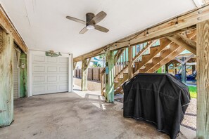 Un espacio exterior techado con ventilador de techo, una parrilla y una escalera de madera.
