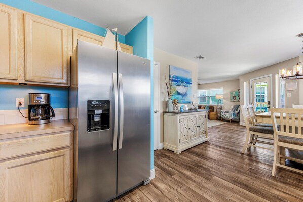 A kitchen with a stainless steel refrigerator, wooden cabinets, a coffee maker, and a dining area with a table and chairs.