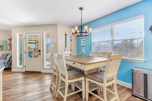 A dining area with a wooden table and chairs, a chandelier, and a window with blinds.