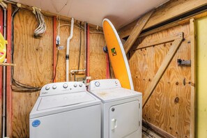 A laundry room with a Whirlpool washer and dryer, wooden walls, and exposed electrical wiring.