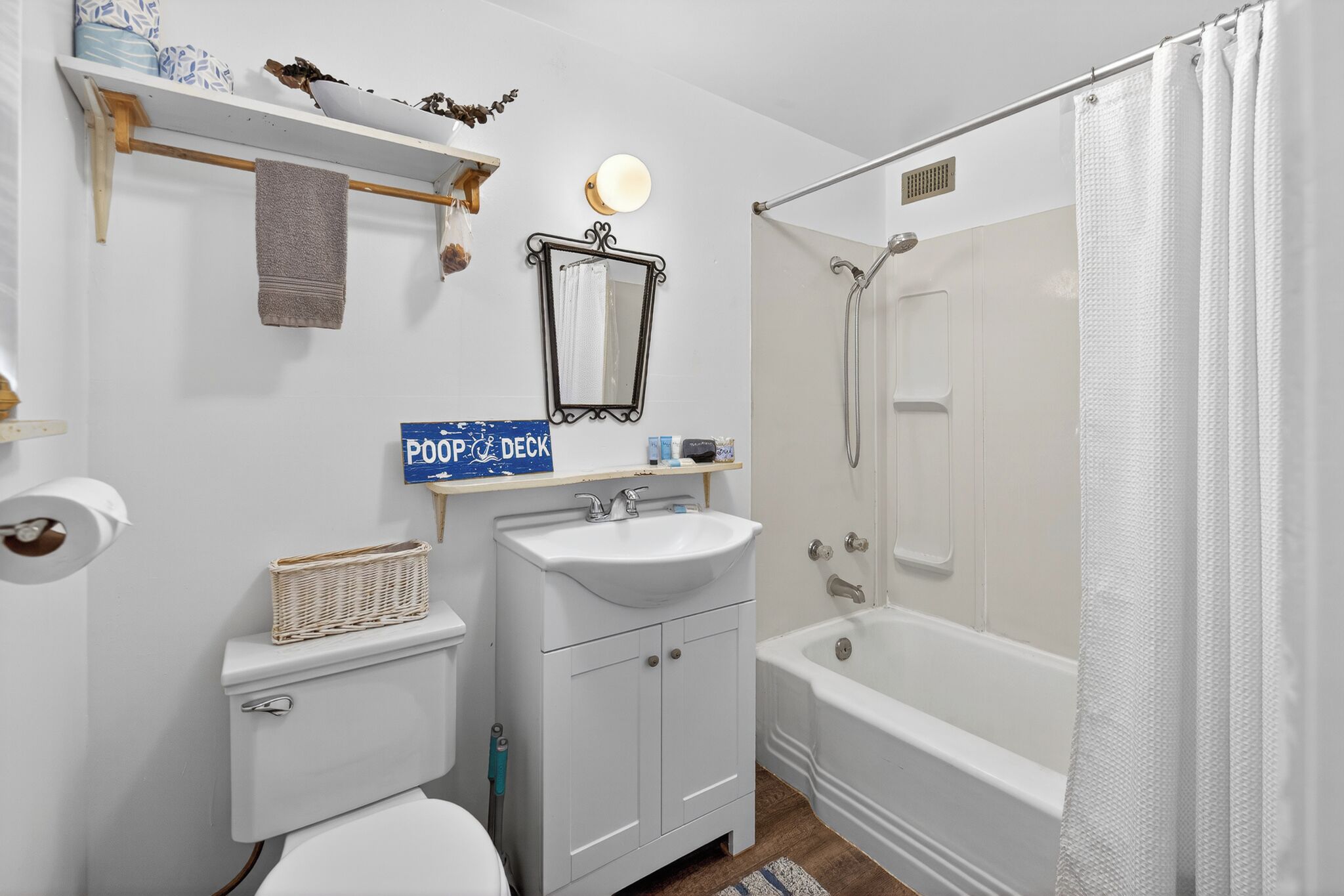 A bathroom with a toilet, sink, mirror, shower, and a 'PooPoo Deck' sign.