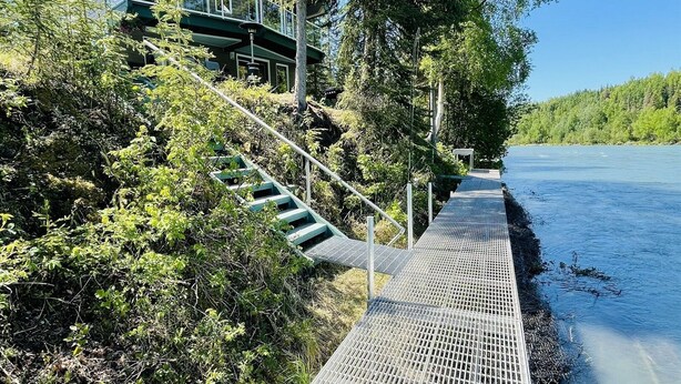 Eine Uferpromenade mit Metallgeländer, Treppen zu einem Gebäude mit Gründach und dichter Bepflanzung.