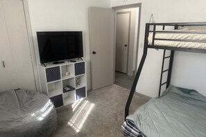 A room with a bunk bed, a television on a stand, a storage unit, and a door leading to another room.