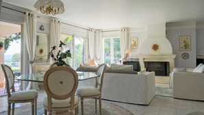 Ein geräumiges Wohnzimmer mit einem Glastisch, bequemen Sitzmöglichkeiten, einem Kamin und großen Fenstern.
