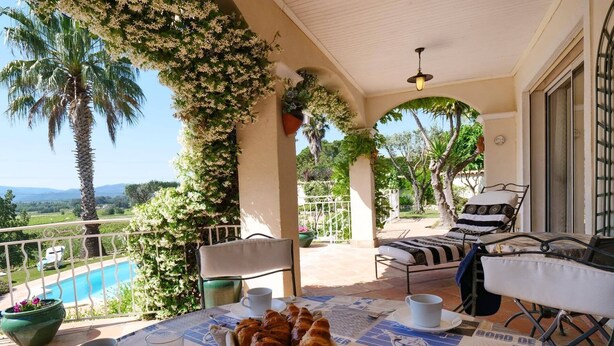 Ein Balkon mit Frühstückstisch, Blick auf den Pool und eine Palme.
