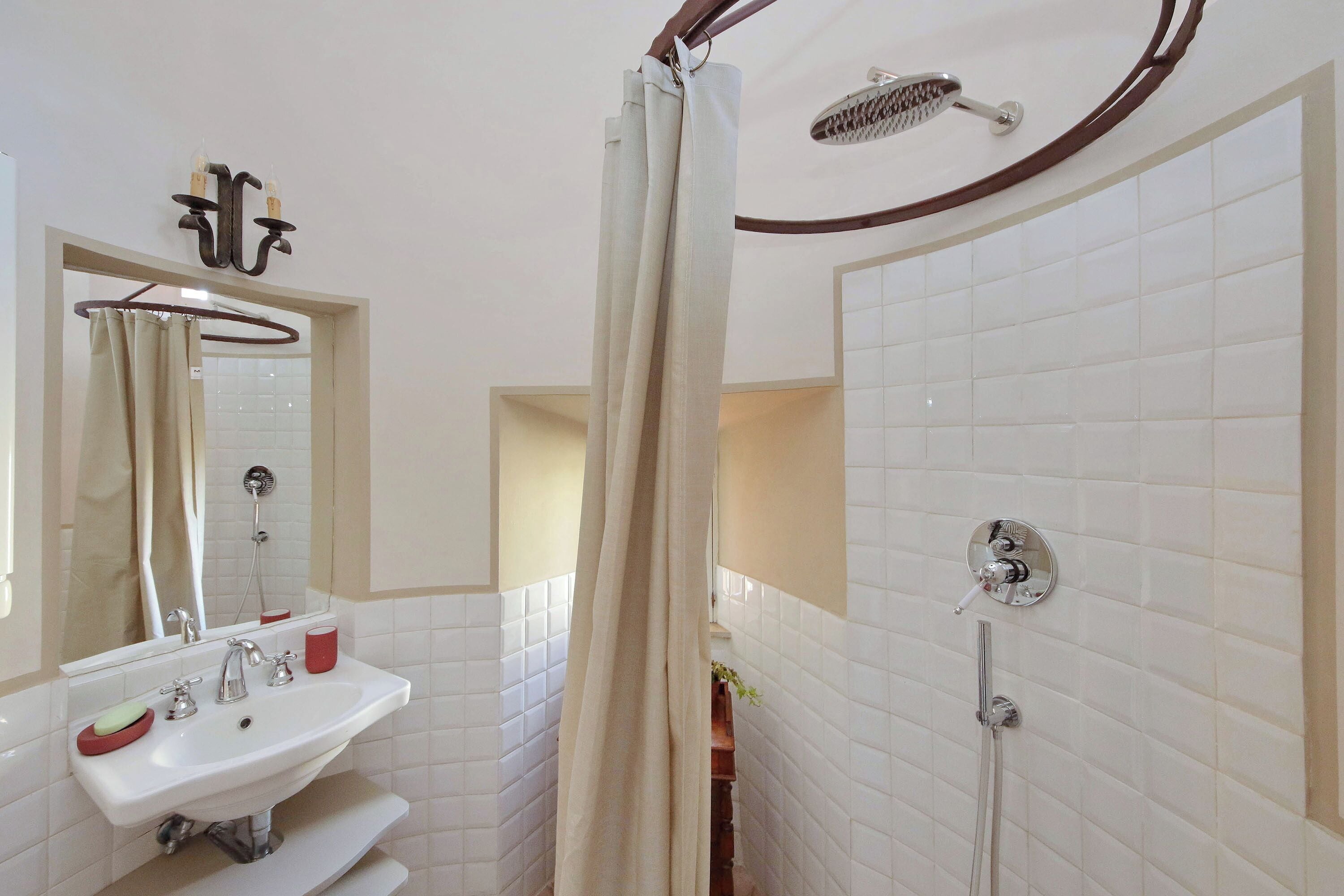 Un bagno con lavandino bianco, specchio e doccia con tenda.
