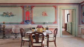 A dining area with a table set for four, chairs, a vase with flowers, and a decorative ceiling with frescoes. - Hotel PalazzoVittoria HeritageCollection (Cerveteri)