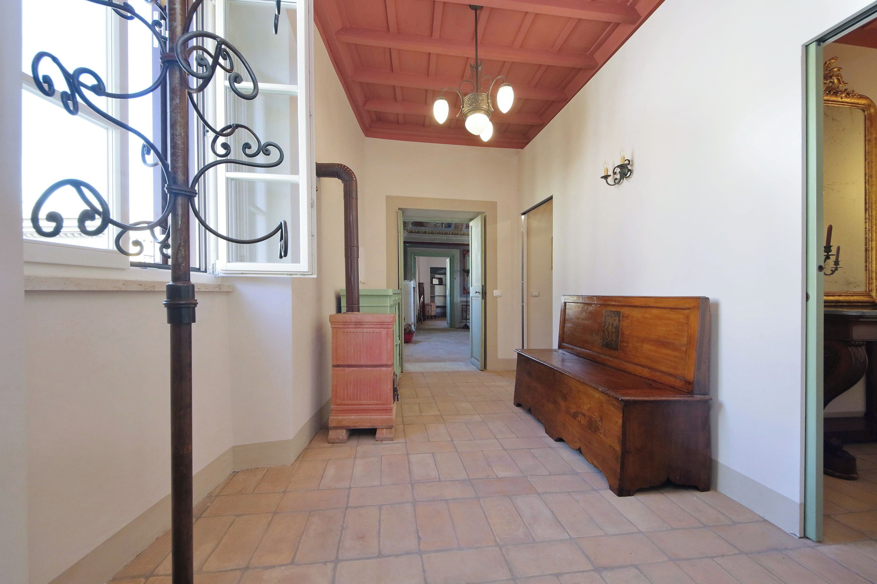 Un couloir avec un banc en bois, un poteau en métal et un miroir.