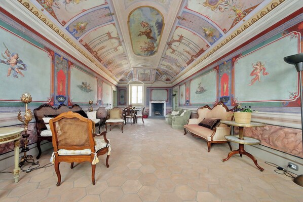 Una habitación con frescos decorativos en el techo, muebles antiguos y una chimenea.