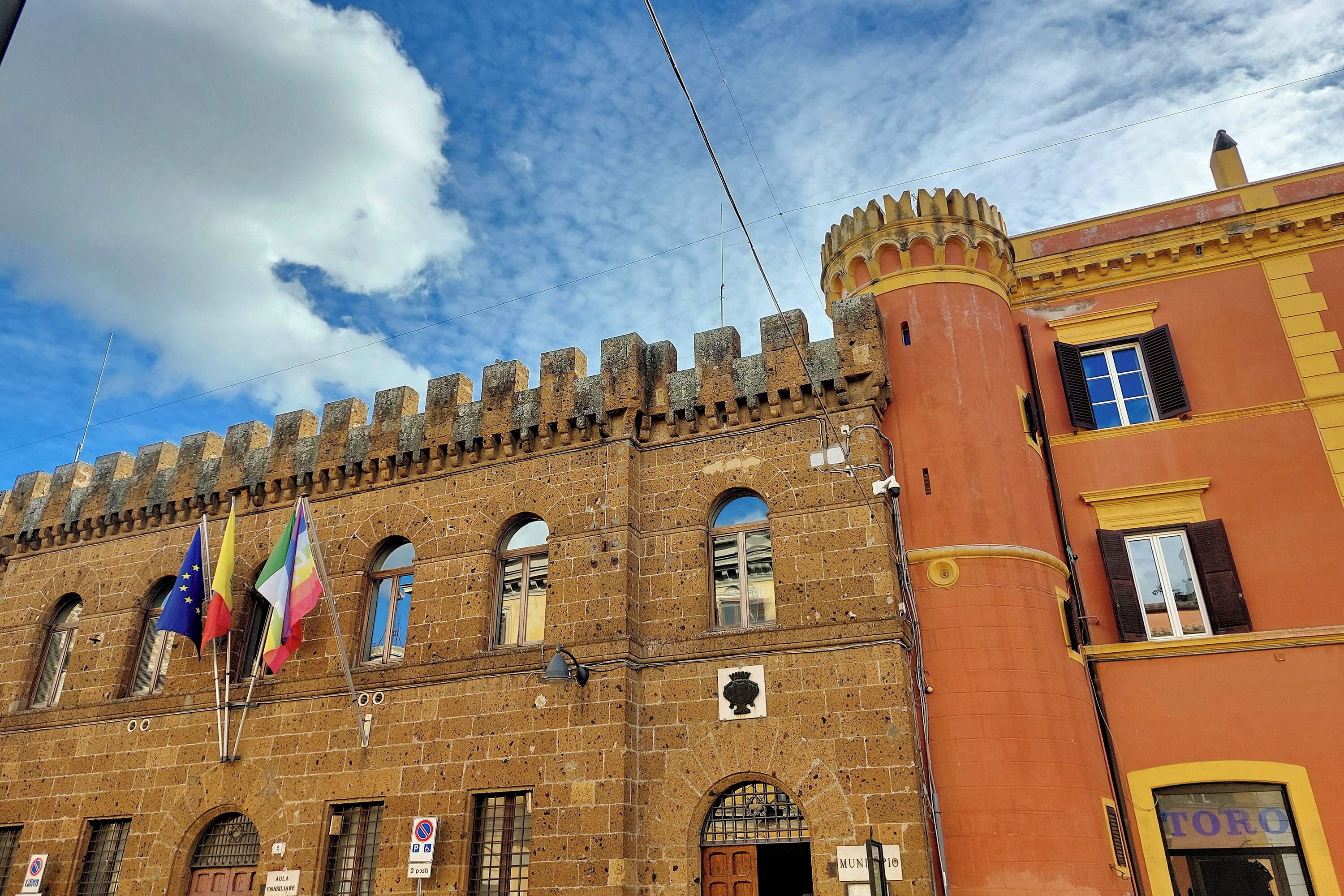 Un edificio storico con una torre imponente, finestre ad arco e bandiere.
