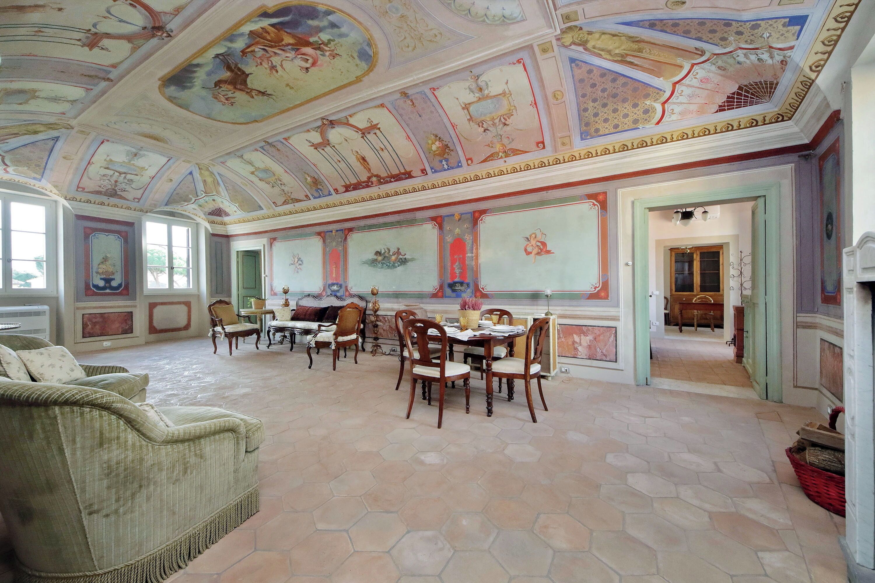 A room with a hexagonal tiled floor, a dining table with chairs, a sofa, and a ceiling with painted murals.