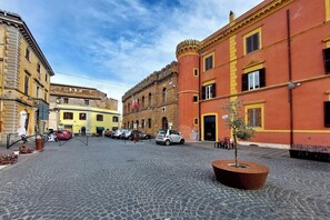 Una calle adoquinada con edificios históricos, una jardinera pequeña y coches aparcados.