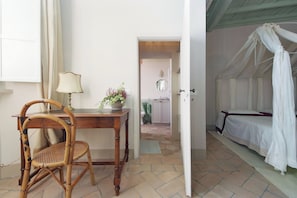 Una habitación con una cama, una silla, una mesa con una lámpara y una puerta que da a otra habitación.