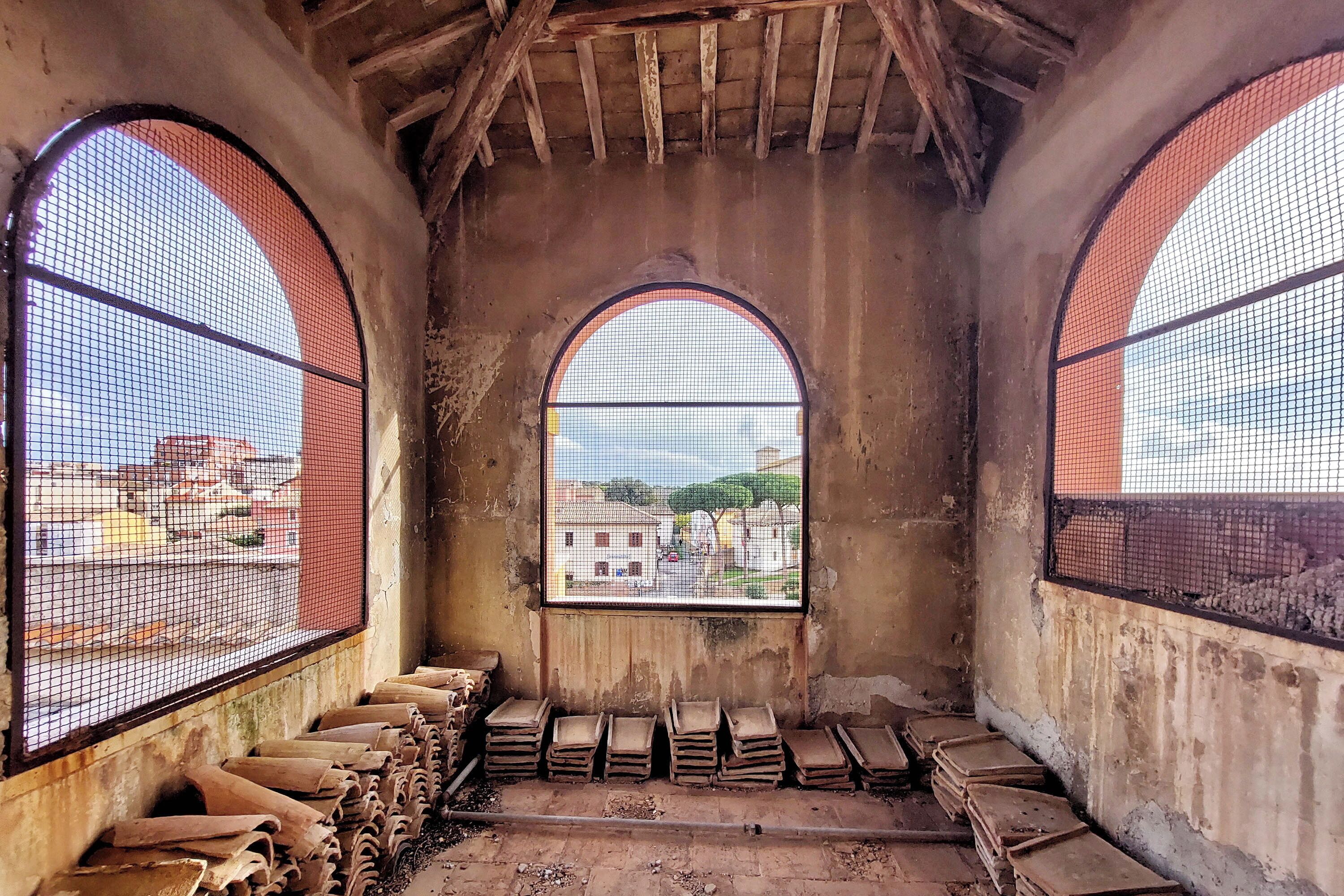 An interior with arched windows, a concrete floor, and stacks of flat objects.