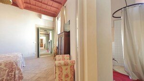 A hotel room with a bed, a chair, a bathroom with a shower curtain, and a hallway leading to another room. - Hotel PalazzoVittoria HeritageCollection (Cerveteri)