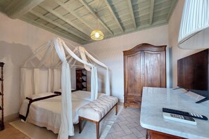 Un dormitorio con una cama con dosel, un armario de madera, una mesita de mármol con un control remoto y un ventilador de techo.