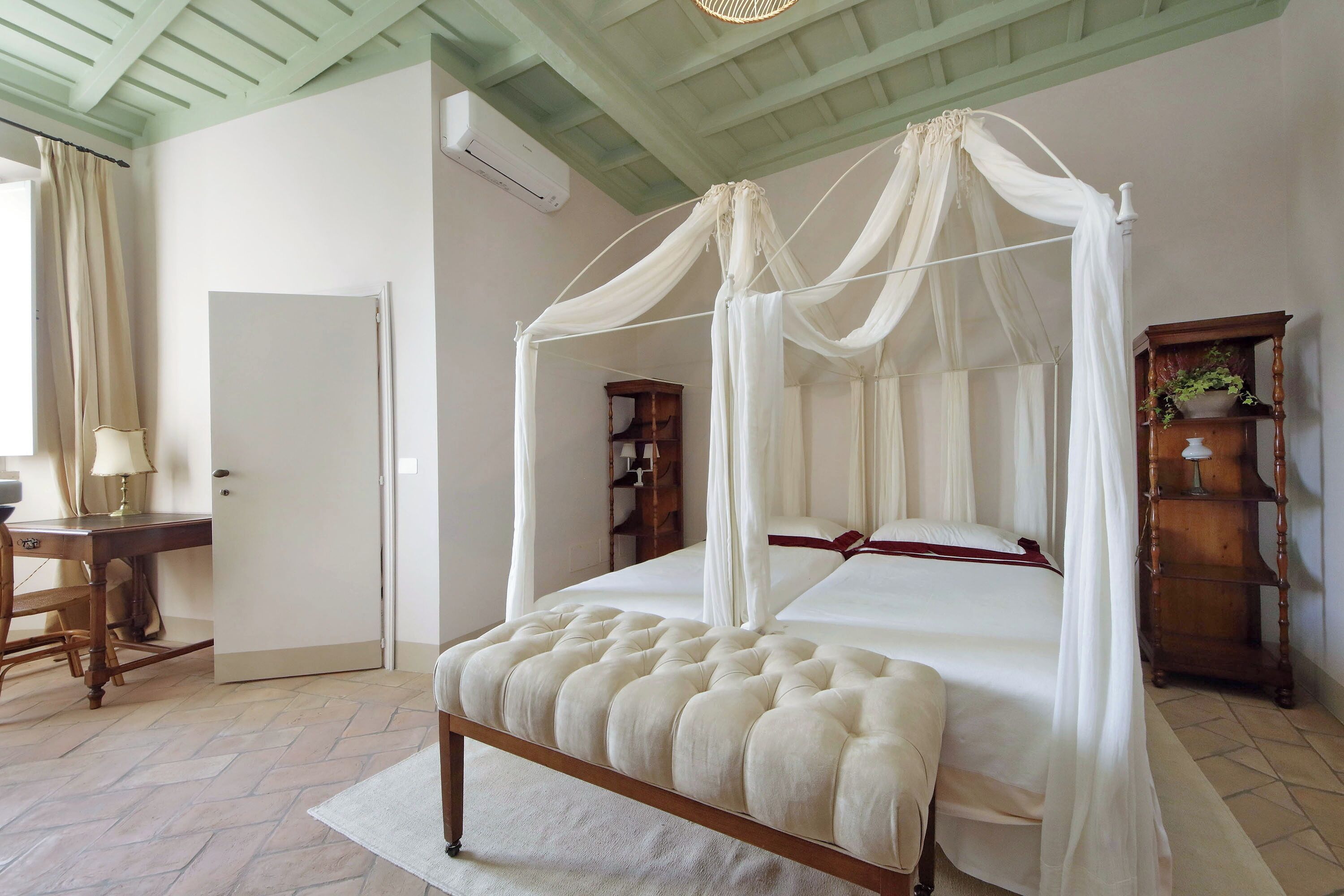 Een slaapkamer met een hemelbed, een houten bankje, een bureau en een kledingkast.