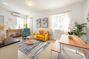 Ein Wohnzimmer mit einem gelben Sofa, einem blauen Sessel, einem runden Couchtisch und einem Holznachttisch.