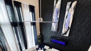 Un salon moderne avec un canapé d’angle, un tapis à motifs et un mur foncé à la texture intéressante, agrémenté d’œuvres d’art.