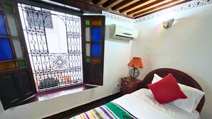Ein Hotelzimmer mit Bett, Nachttisch, Lampe, Klimaanlage und einem Fenster mit Ziergitter.