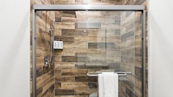 A shower with a glass door, wooden tiles, a towel rack, and a toilet visible to the right.