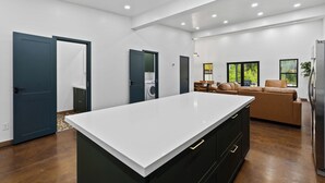 A modern kitchen with a large island, dark cabinetry, and a dining area with a sofa and table. - Glacier Luxury Retreat / Green Olive Apartment 1 (Hungry Horse)