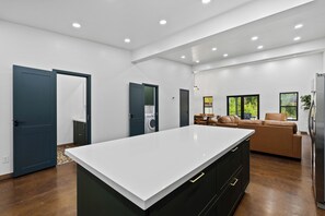 Une cuisine moderne dotée d’un grand îlot central, de meubles de rangement aux couleurs sombres et d’un coin repas avec un canapé et une table.
