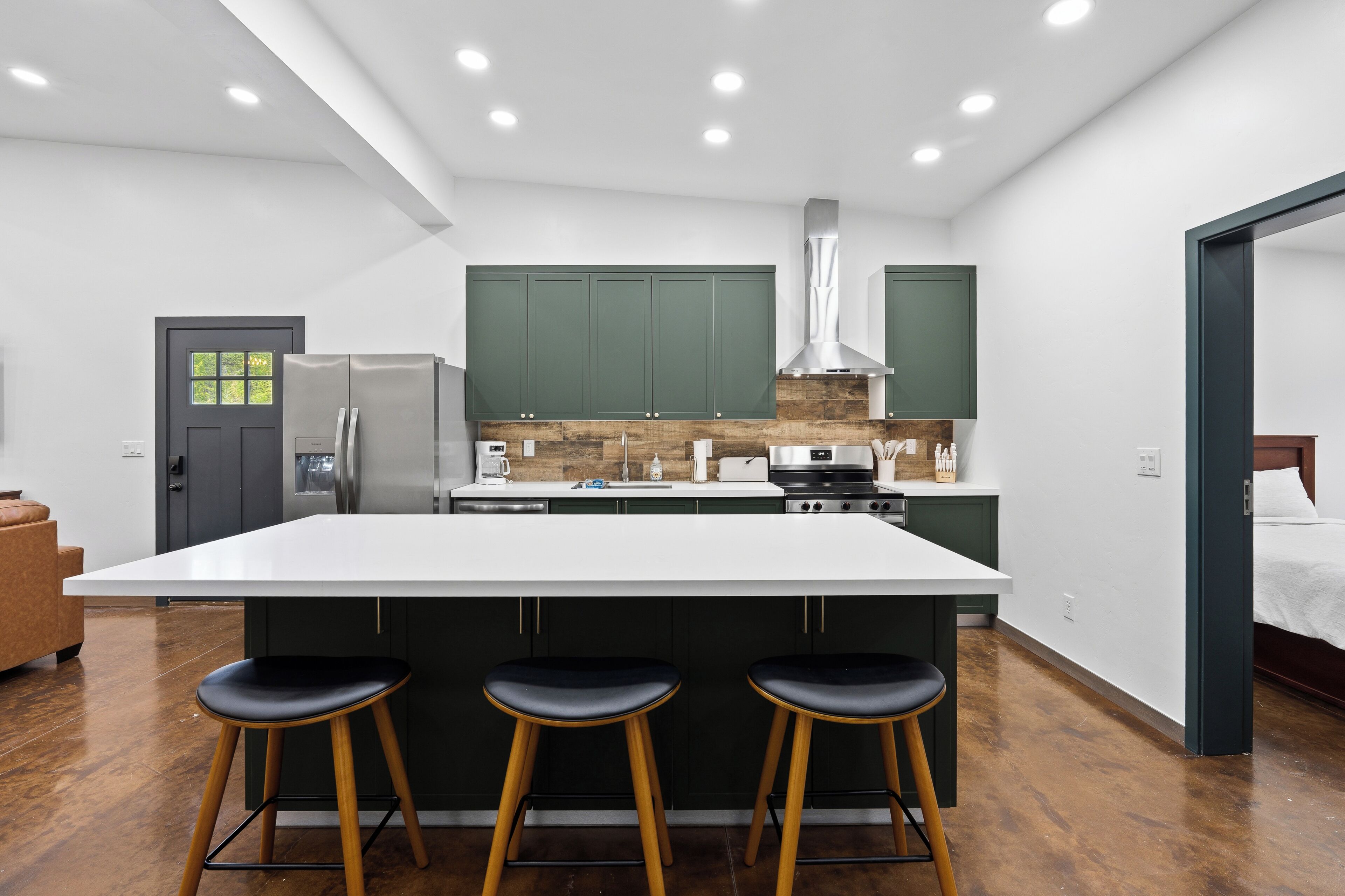 Una cucina moderna con una grande isola, sgabelli da bar e mobili verdi.