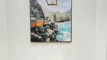 A dining area with a wooden table and chairs, a painting of a train on a cliff, and a hanging light fixture.