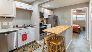 A compact kitchen with a wooden island, white cabinets, stainless steel appliances, and a red towel on the counter. - Lakefront Escape~Dock Access~Patio~Lake LBJ (Kingsland)