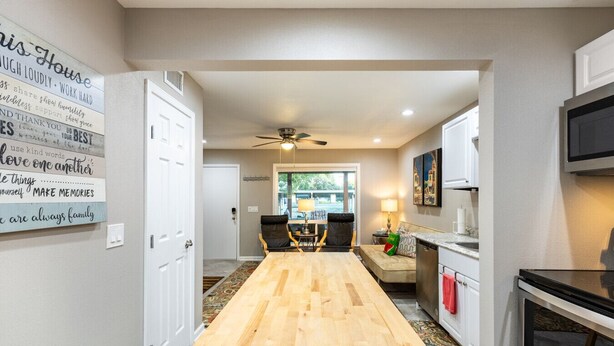 A modern kitchen with a wooden floor, a ceiling fan, and a dining area with a table and chairs. - Lakefront Escape~Dock Access~Patio~Lake LBJ (Kingsland)