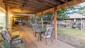 An outdoor covered patio with a table and chairs, a stone wall, and a view of a residential area with a boat. - Lakefront Escape~Dock Access~Patio~Lake LBJ (Kingsland)