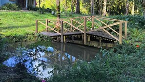 A wooden bridge over a pond with lush greenery and a house in the background. - Rancho Quemeninho - A refuge in the Atlantic Forest in the heart of PETAR. (Apiaí)