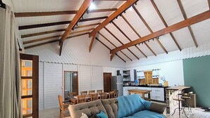 A spacious living area with a high ceiling, wooden beams, a sofa with cushions, a dining table with chairs, and a kitchen area. - Rancho Quemeninho - A refuge in the Atlantic Forest in the heart of PETAR. (Apiaí)