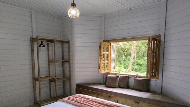 A bedroom with a bed, a window seat, a wooden ladder, and a hanging light fixture. - Rancho Quemeninho - A refuge in the Atlantic Forest in the heart of PETAR. (Apiaí)