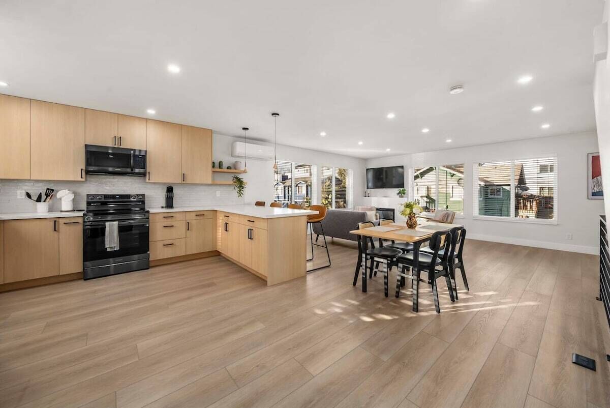Une cuisine moderne avec des meubles en bois, un four encastré et un coin repas comprenant une table et des chaises.
