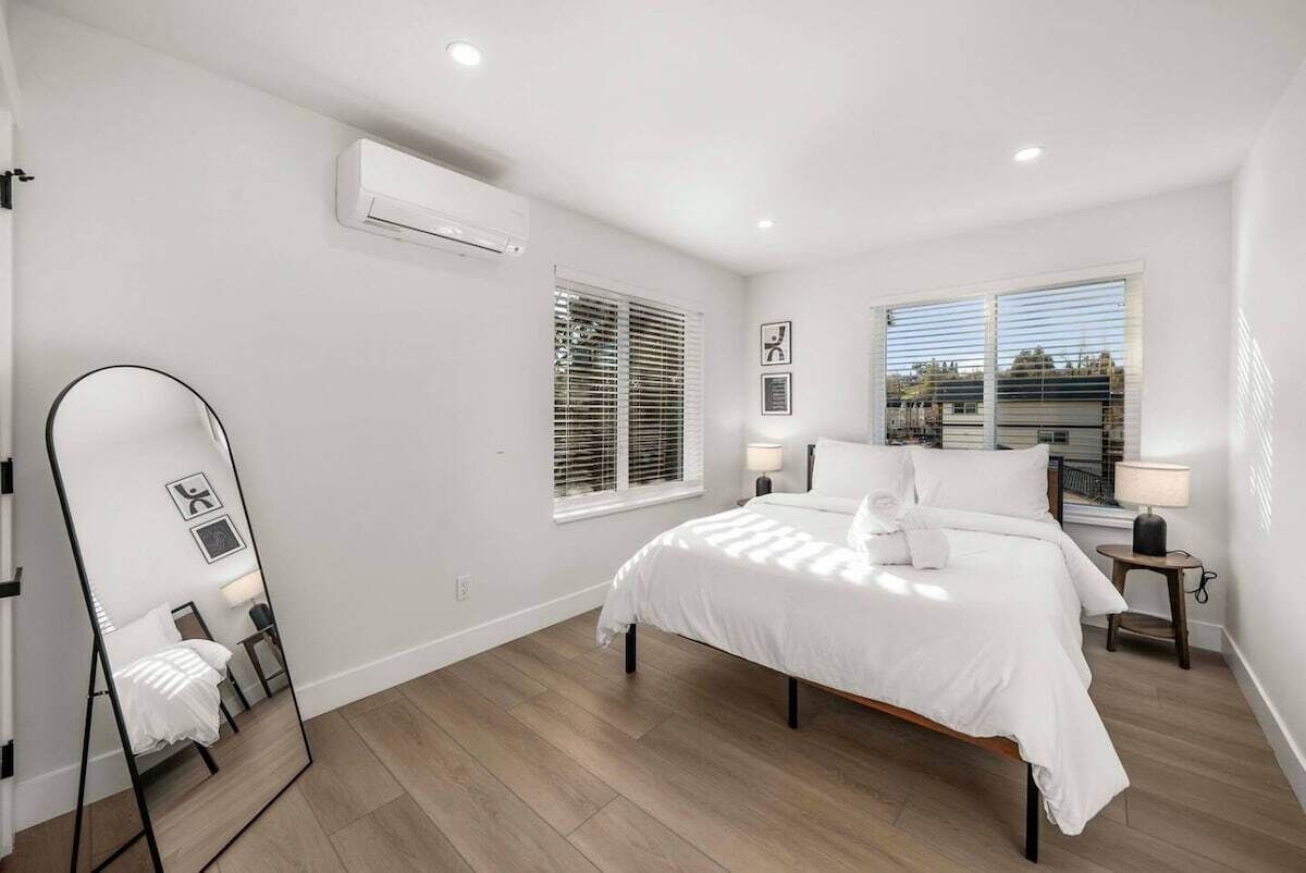 Une chambre à coucher comprenant un lit, un miroir, deux tables de chevet et une fenêtre avec des stores.
