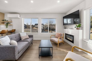 A modern living room with a sofa, chairs, a coffee table, a fireplace, and a TV mounted on the wall. - Brand New 3BR Townhome - Near Light Rail and Airport (Seattle)