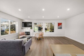 A modern living room with a sofa, armchair, and a TV mounted on the wall. - Brand New 3BR Townhome - Near Light Rail and Airport (Seattle)